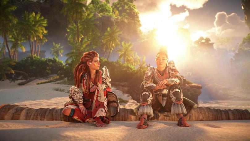 Aloy and Seyka sitting on a log on the beach with a sunrise behind them. Both are having an emotional conversation.